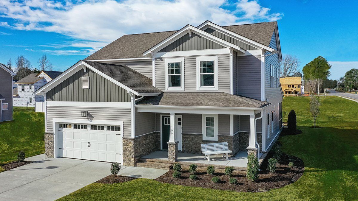 Two-story gray house with white garage door and front porch, set on a green lawn under a blue sky.
