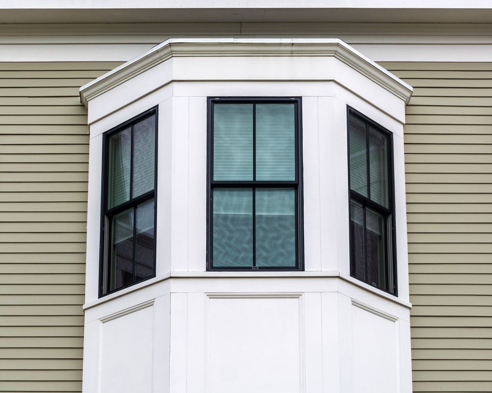 White bay window with three black-framed windows on tan building exterior.