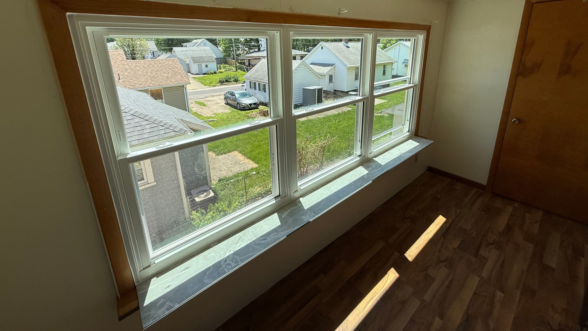 Empty room with a large window, wood floor, and sunlight streaming in onto the floor.