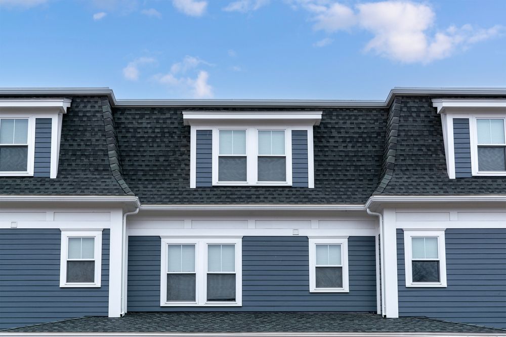 Blue house with gray roof and multiple white-framed windows against a blue sky.