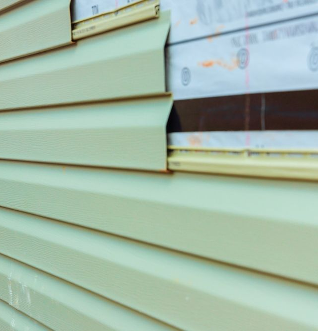 A person installing pale green vinyl siding on a building's exterior.