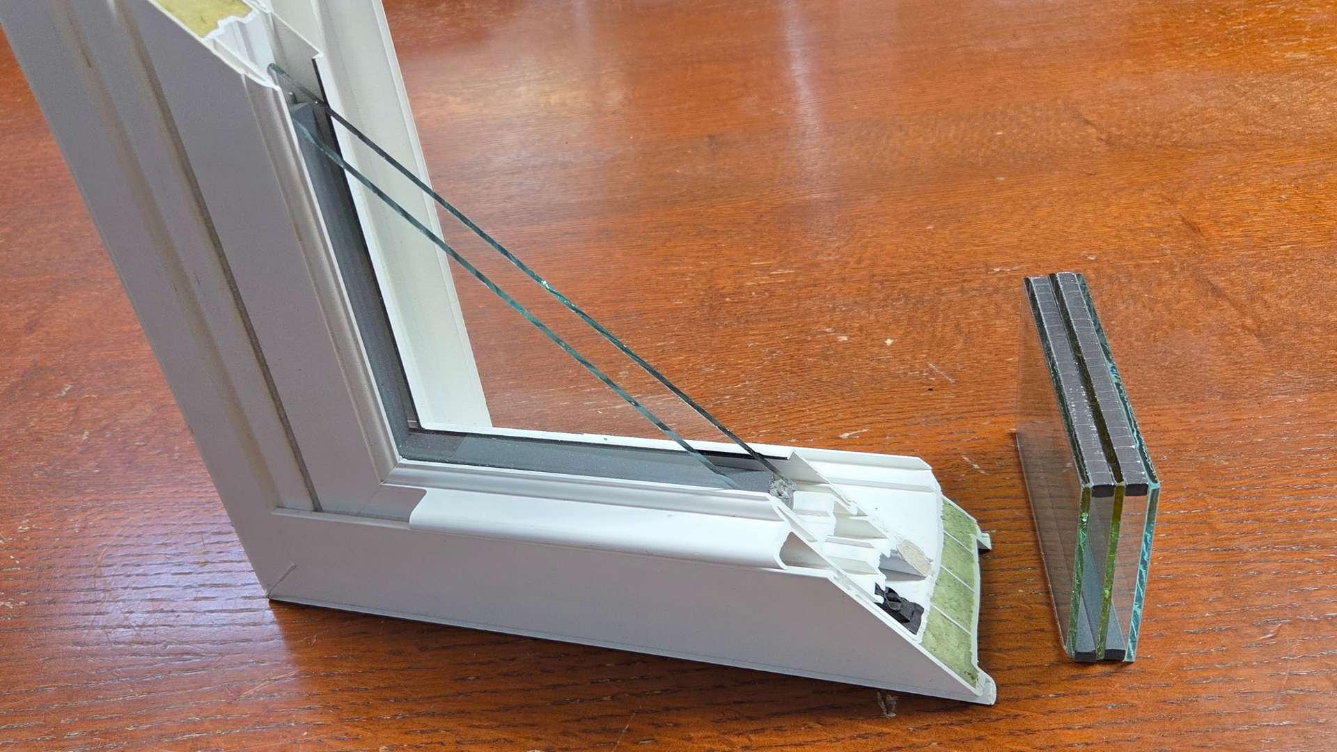 White window frame corner with a, next to a small triple pane sample and super spacers on a wooden surface
