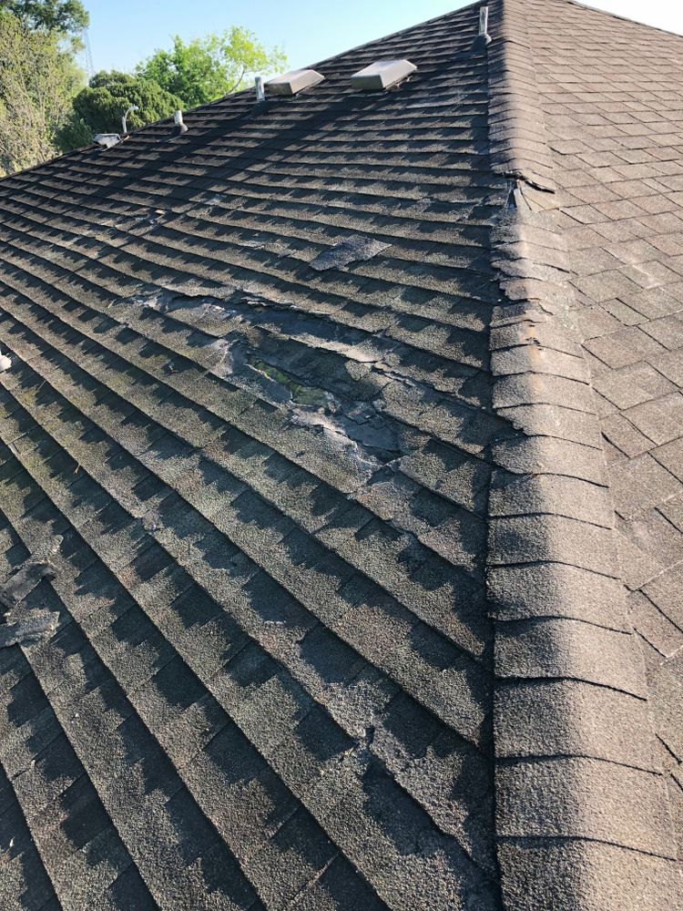 Overhead view of a dark asphalt shingle roof, with a large area of damaged, missing shingles.