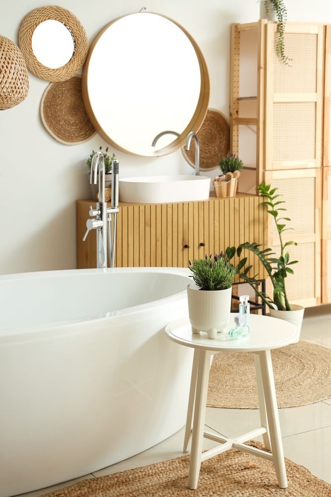 Bathroom with a white bathtub, wooden vanity, round mirror, and woven wall decor.