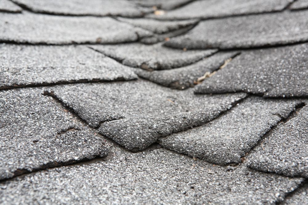 Close-up of weathered gray asphalt roof shingles with a rough, textured surface.