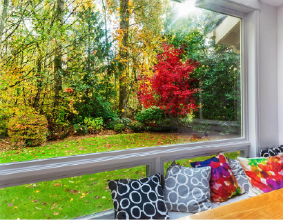 A window seat with colorful pillows, overlooking a vibrant autumn garden with red and green trees.