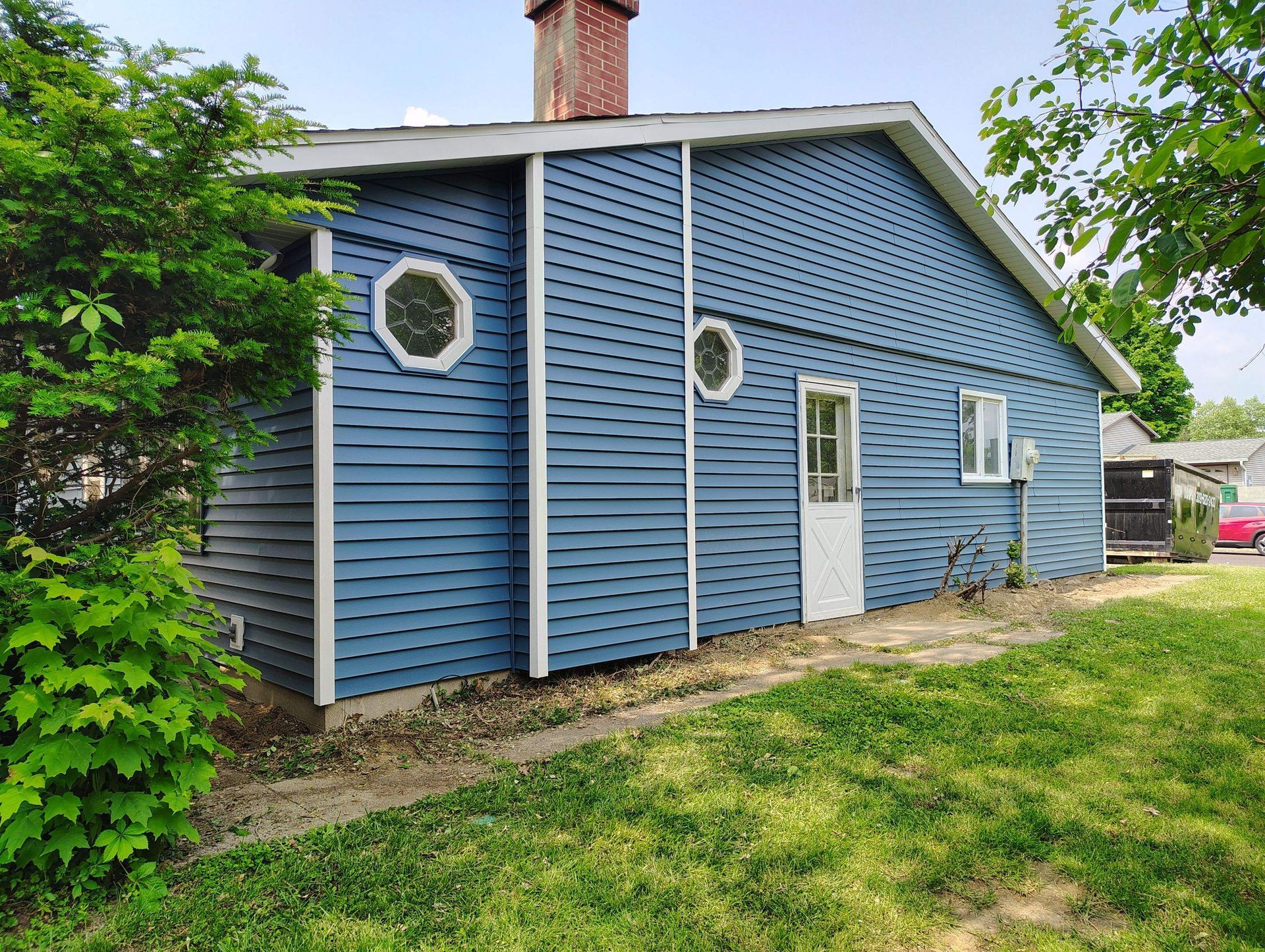 Blue house exterior with round and rectangular windows, white trim, and a grassy yard