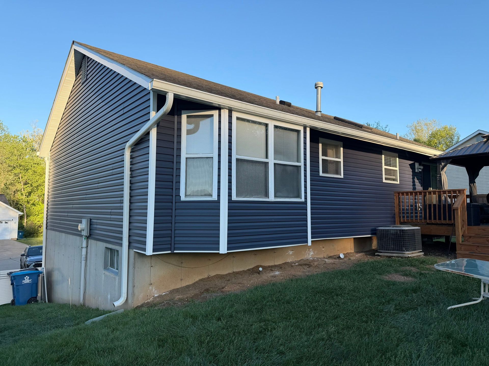Blue house exterior with white trim, sloped roof, and a small deck on the right side.