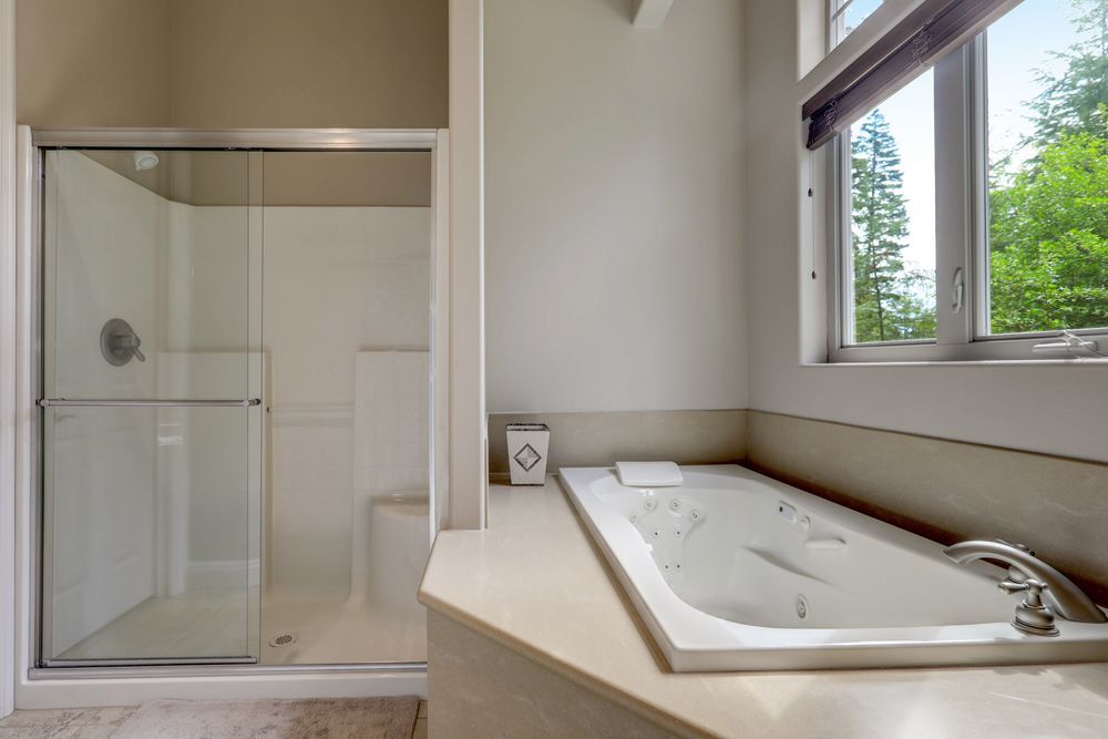Bathroom with a glass shower, a rectangular bathtub, and a window with a view of trees.