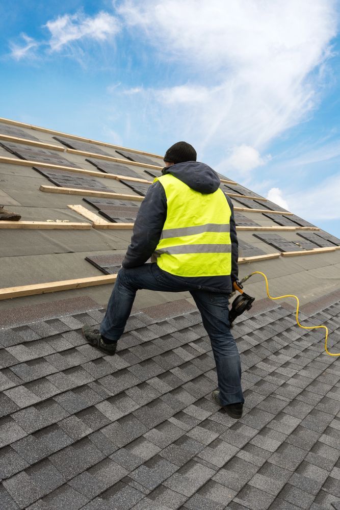Roofer wearing a yellow safety vest on a sloped roof with shingles, against a blue sky.