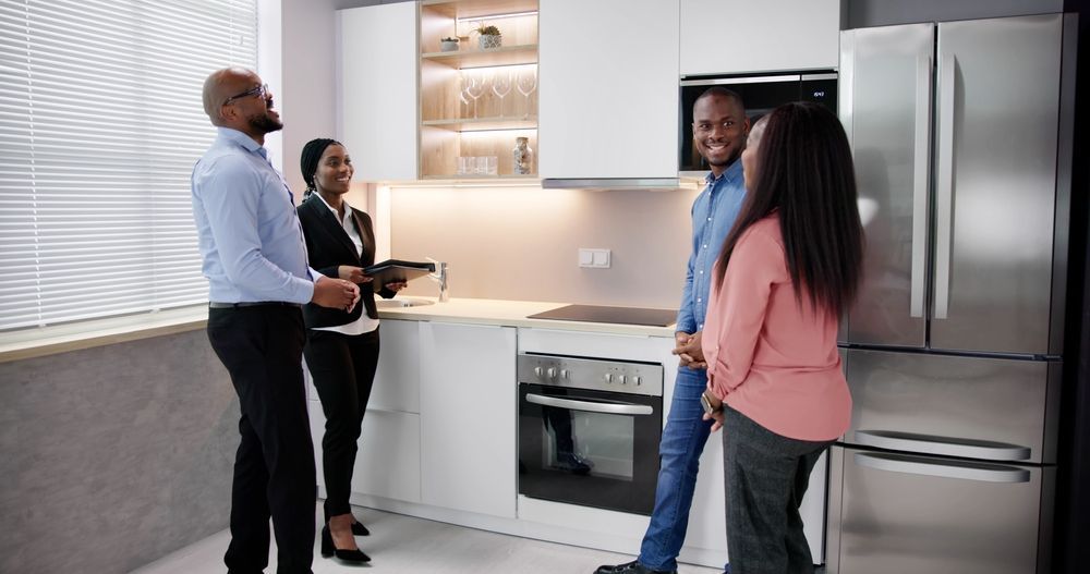 Couple viewing a kitchen with a realtor. Stainless steel appliances, bright cabinets.