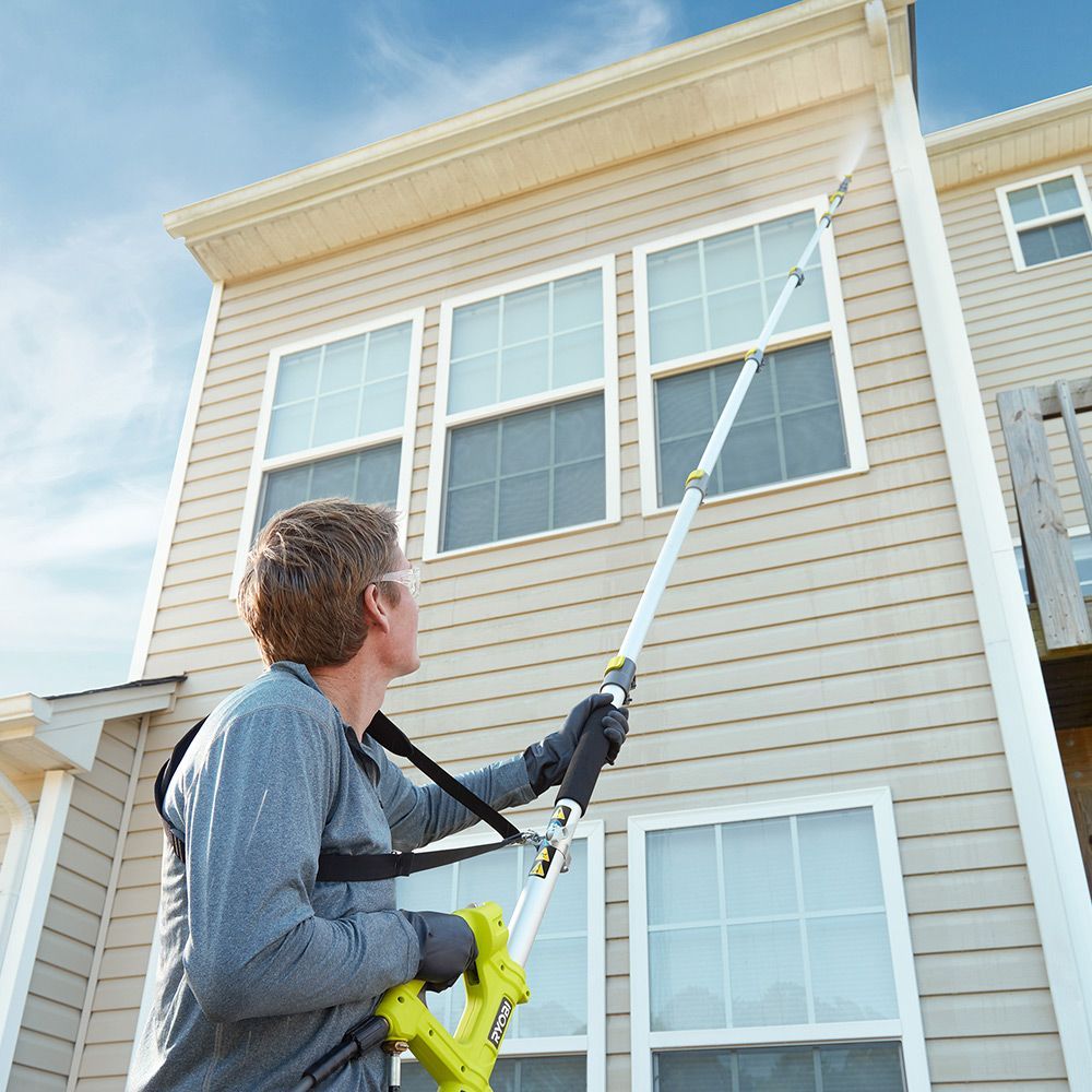 Homeowner cleaning vinyl siding using a soft brush and low pressure water on a residential house.