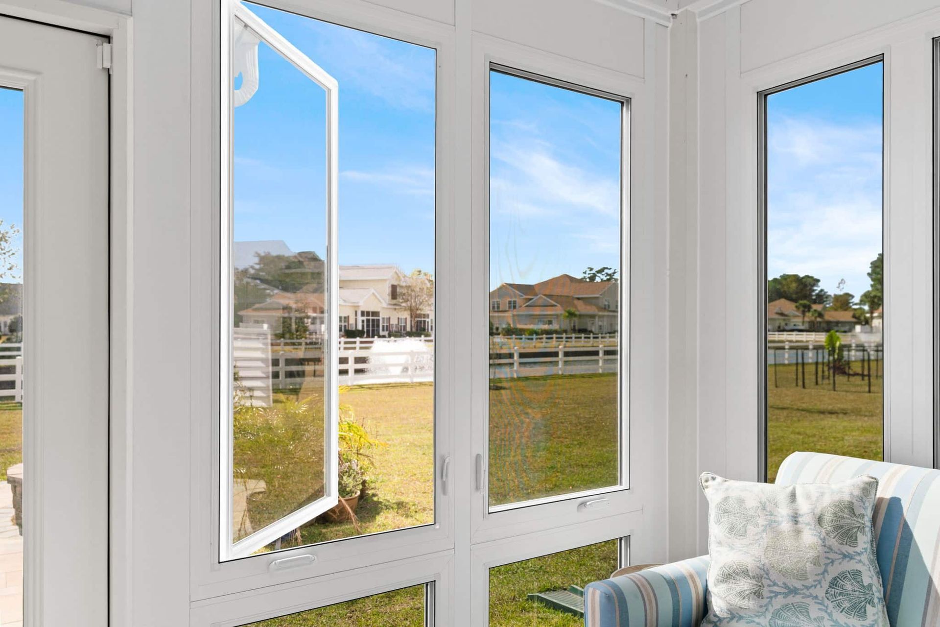 A white-framed window, one open, overlooks a sunny yard and houses.
