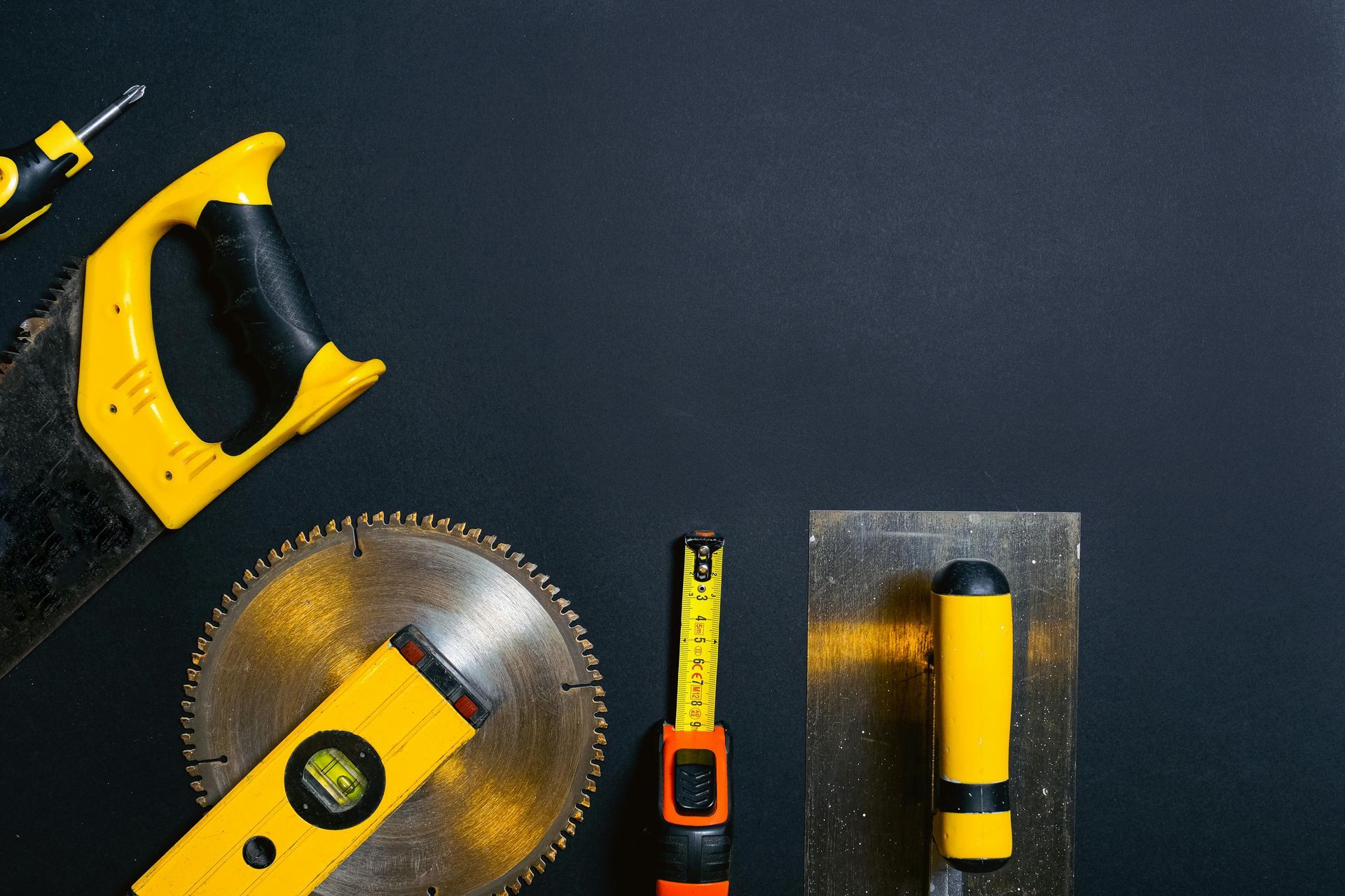 A circular saw , level , tape measure , and trowel are on a black surface.