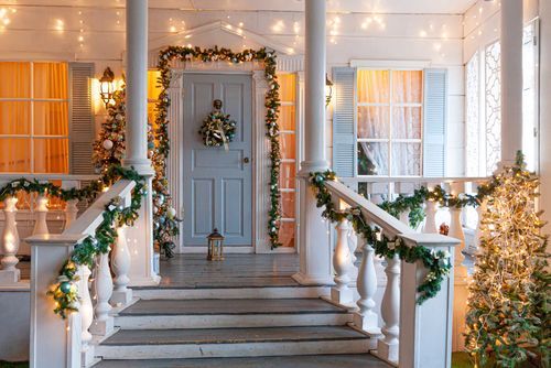A festive porch decorated for Christmas with garland, lights, and a wreath on a blue door.
