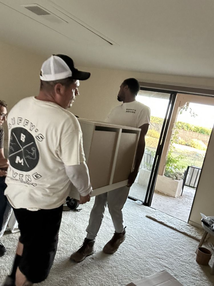 Two people carrying a light-colored cabinet through a doorway, moving furniture.