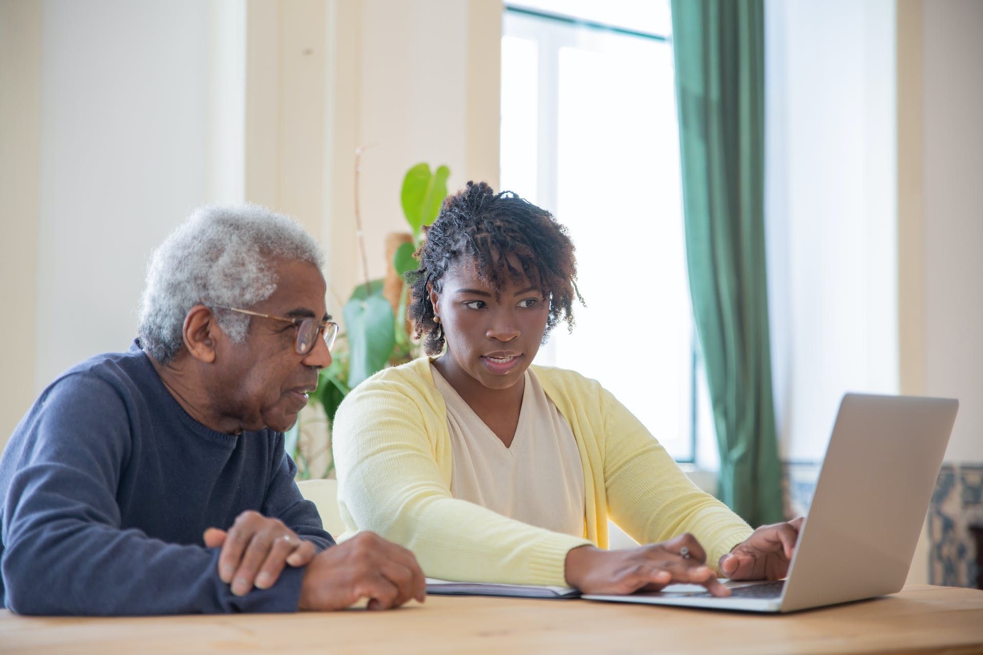 A man and a woman are sitting at a table looking at a laptop computer.