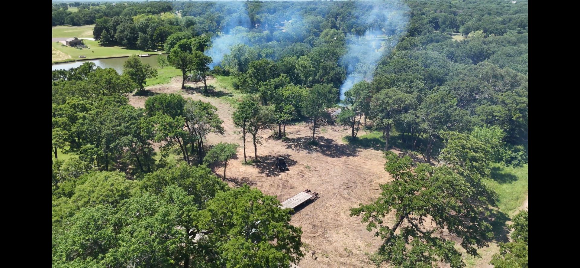 Aerial view of a wooded area with blue smoke rising above the trees.