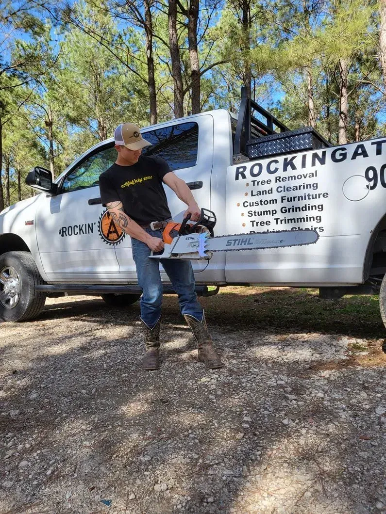 Man with chainsaw in front of a white truck with company name and logo.