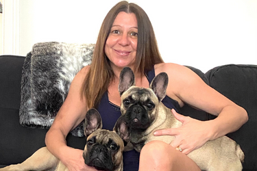 A woman is sitting on a couch with two french bulldogs.