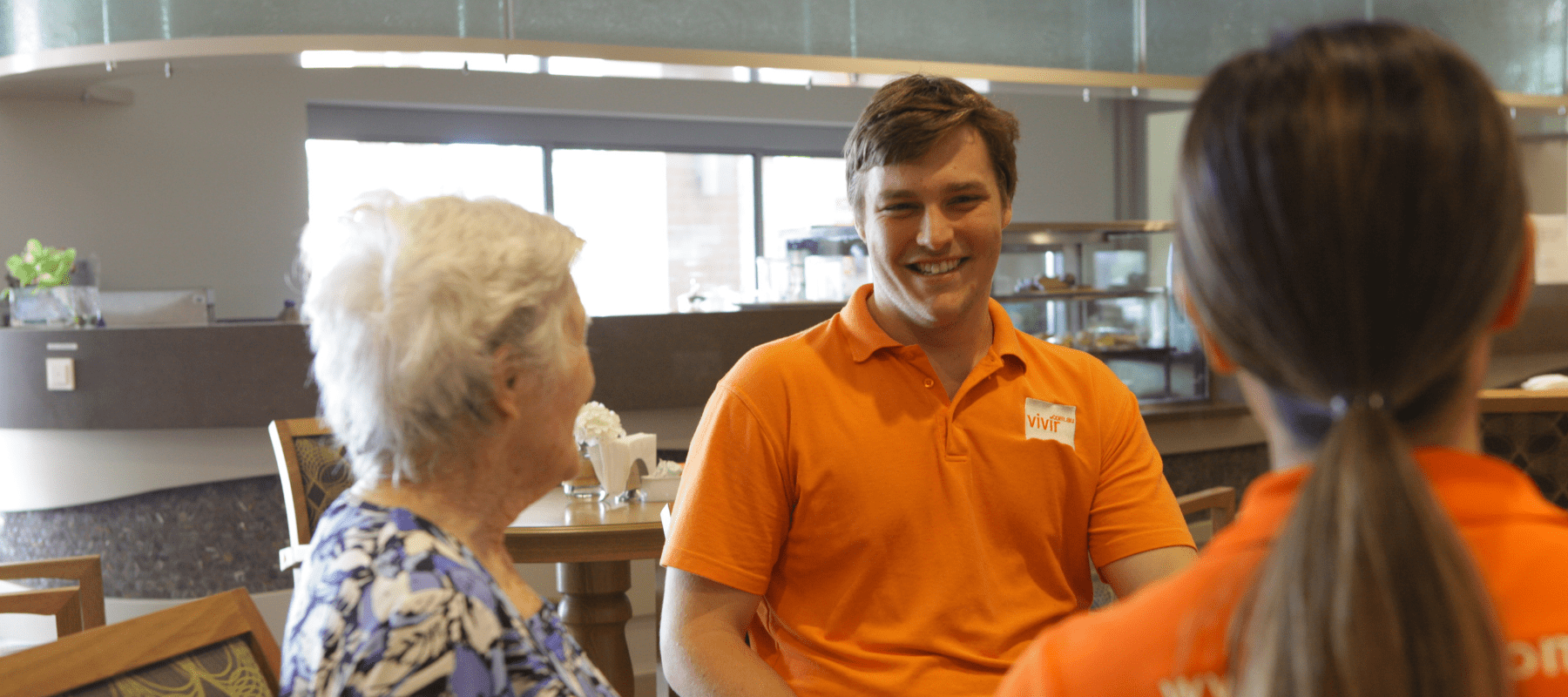 A man in an orange shirt is talking to two women.