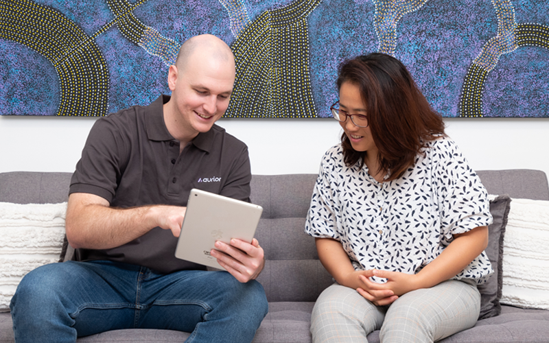 A man and a woman are sitting on a couch looking at a tablet.