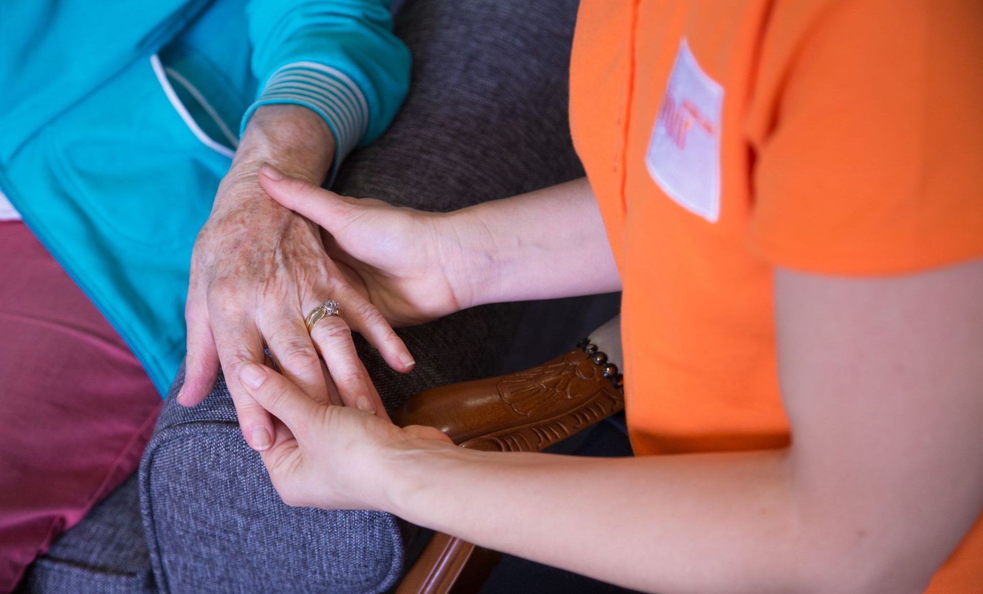 A woman in an orange shirt is holding the hand of an older woman.