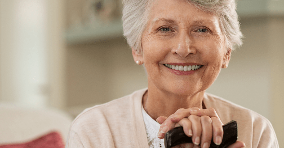 An elderly woman is smiling while holding a cell phone.