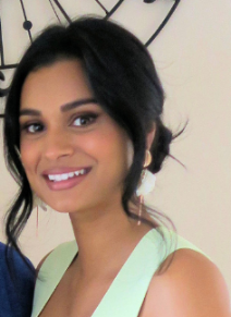 A woman in a green dress is smiling in front of a clock.