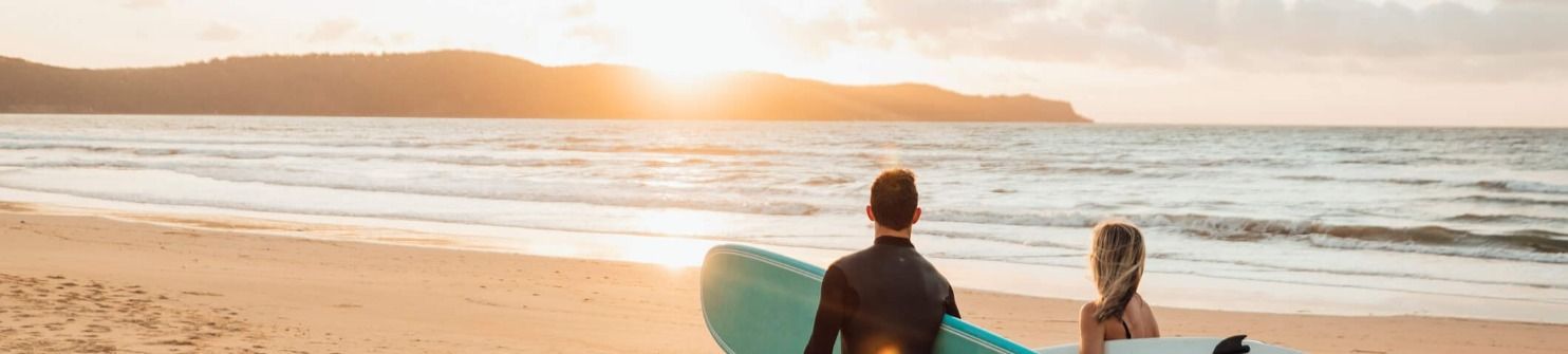 A man and a woman are standing on a beach holding surfboards.