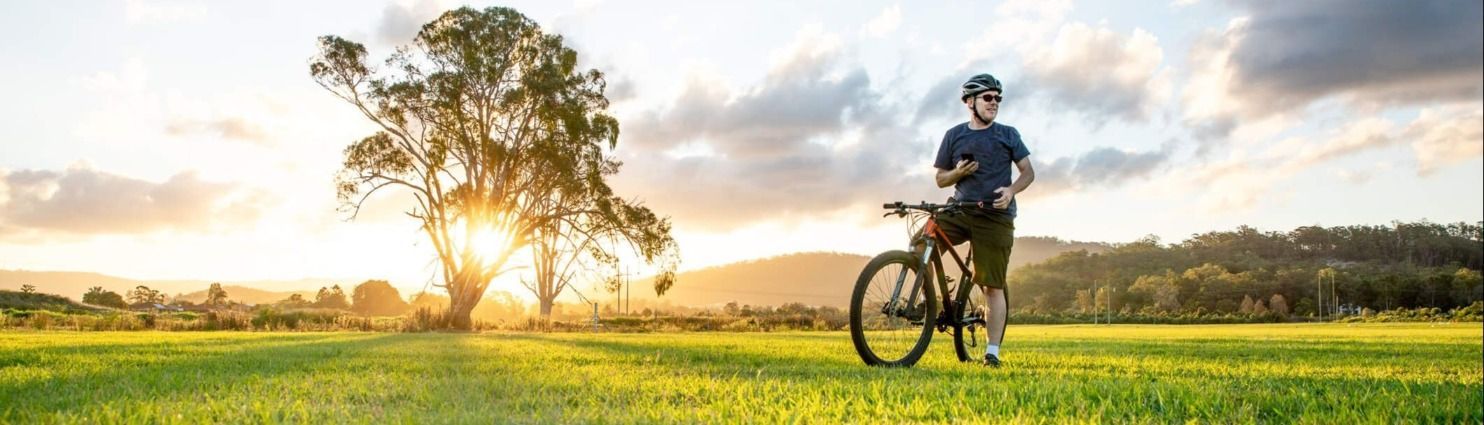 A man is standing next to a bicycle in a grassy field at sunset.