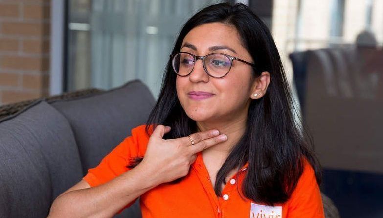A woman wearing glasses and an orange shirt is sitting on a couch.