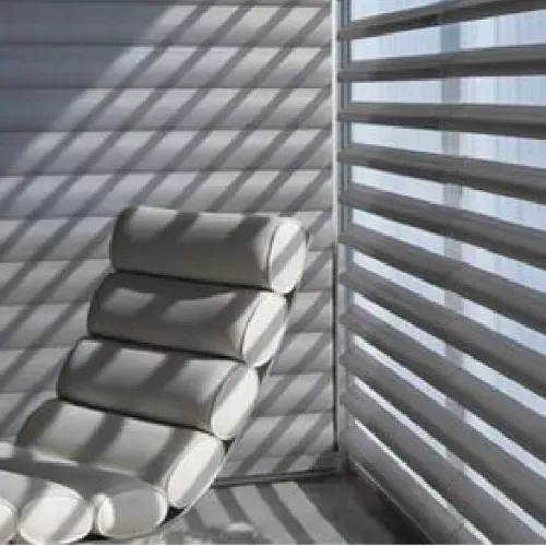 A white chair is sitting in front of a window with blinds.