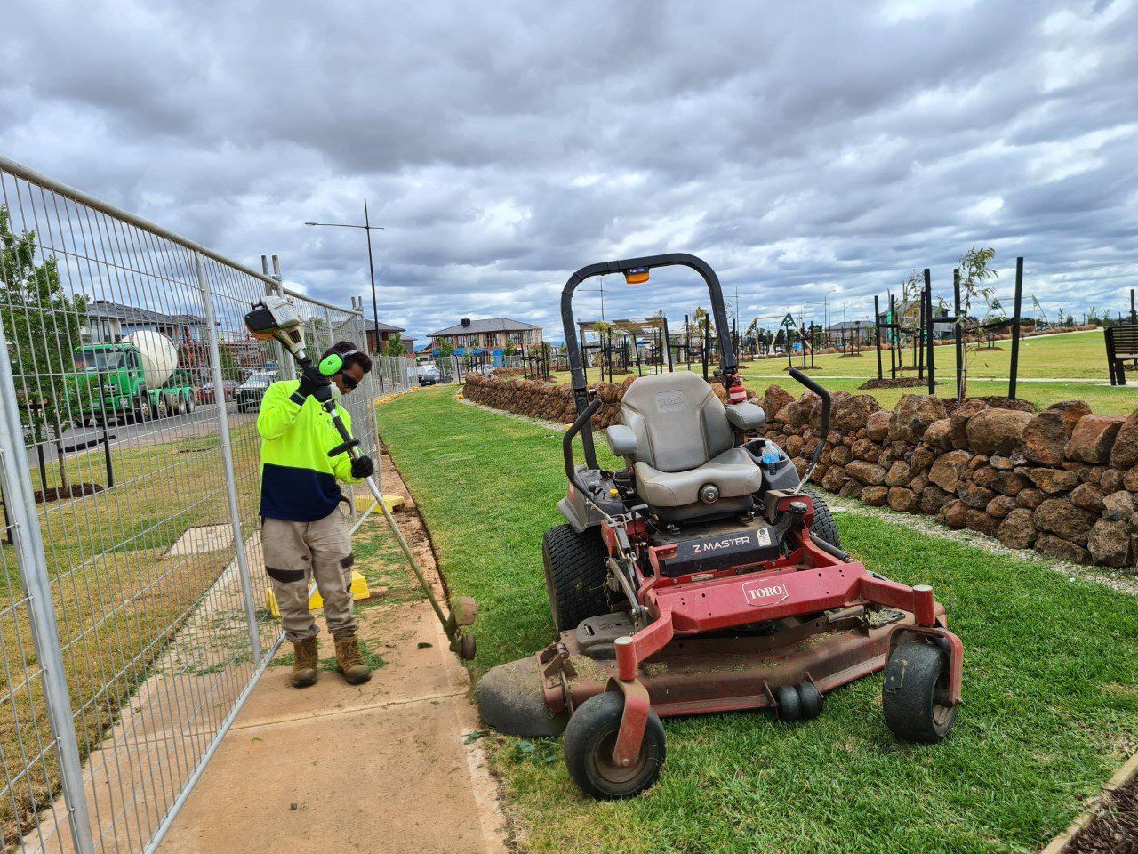 Gardener working next to a ride on mower while using a whipper snipper