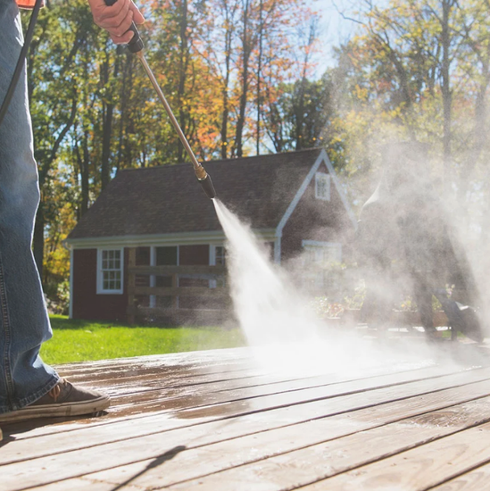 A person is using a high pressure washer to clean a wooden deck
