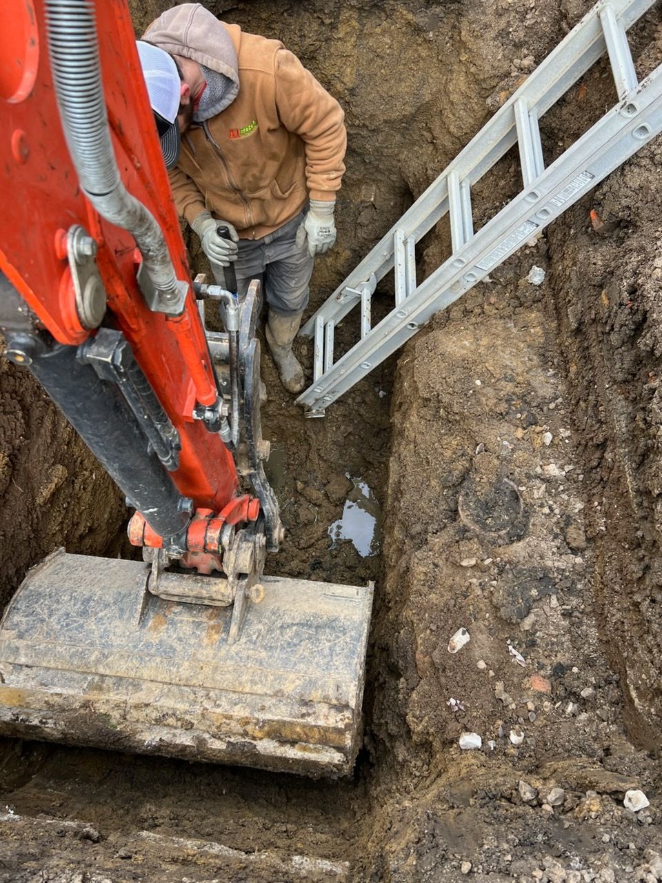 Excavator digging a rectangular pool foundation in red soil, wooden framework around perimeter.