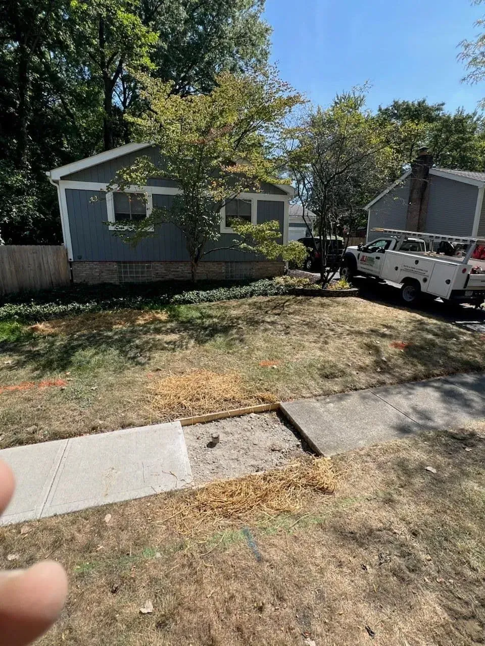 Exterior view of a small blue house, partial sidewalk, dry grass, and a utility truck parked in the yard.