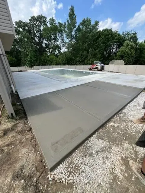Newly poured concrete patio beside a swimming pool, outdoor setting.