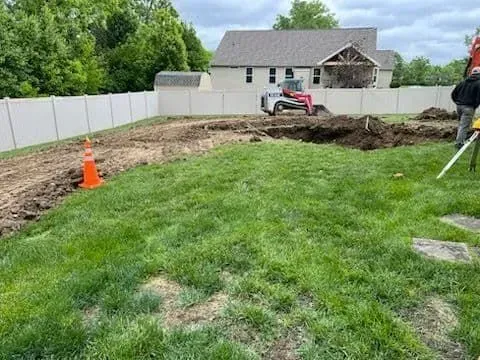 Construction site with a small excavator, fenced yard, and person surveying.