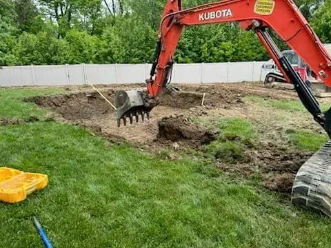 An orange Kubota excavator digging a hole in a grassy backyard.