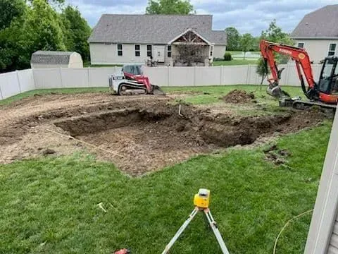 Excavation in progress: A backyard with a hole being dug for a pool. Heavy machinery and surveying equipment visible.