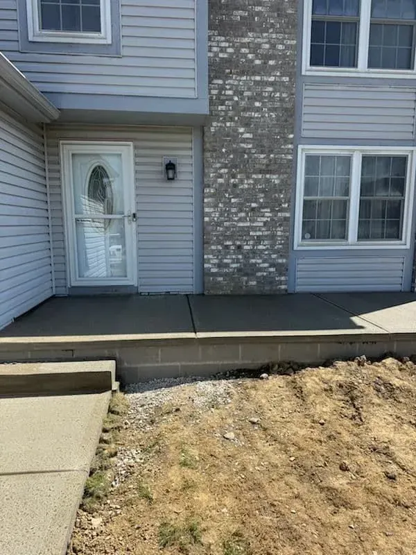 A concrete porch and sidewalk lead to a light-blue sided building with a brick chimney.