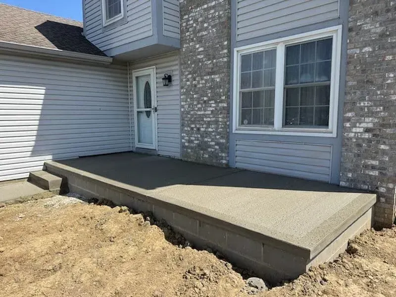 New concrete front porch and steps, next to a home with siding and brick.