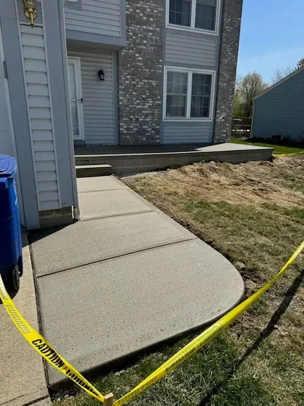 New concrete walkway and steps leading to a two-story house with gray siding. Yellow caution tape is present.