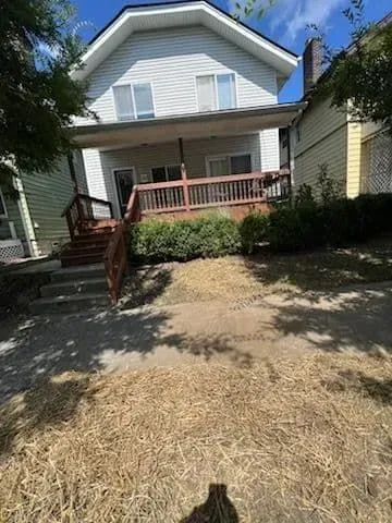 Two-story house with gray siding, porch, and a brown wooden deck. Dry grass in front.