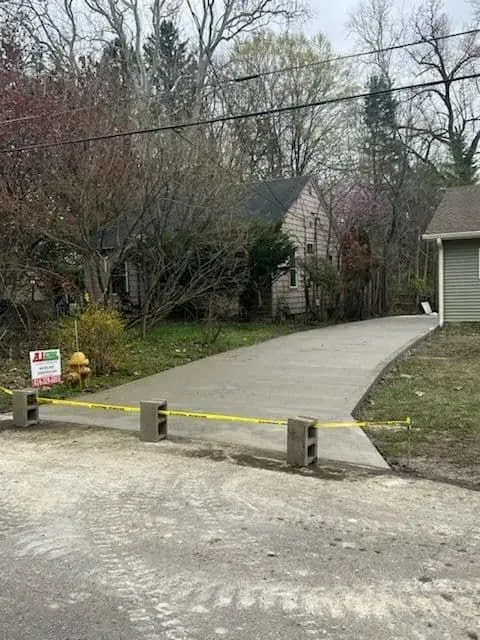 New concrete driveway blocked by cinder blocks and yellow tape; house in the background.