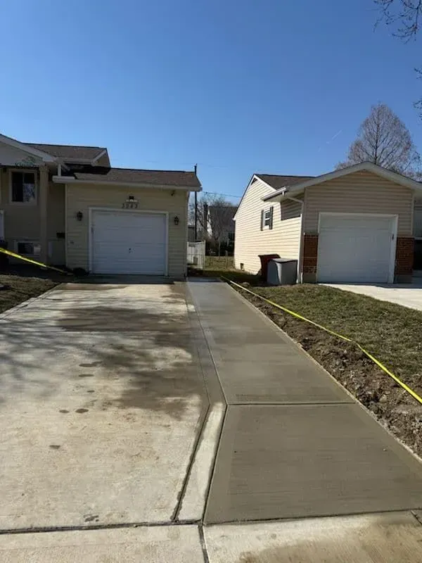 Newly poured concrete driveway between two houses with garages, bright sunny day.