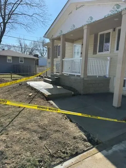 Newly constructed home with concrete steps and porch, surrounded by yellow caution tape.