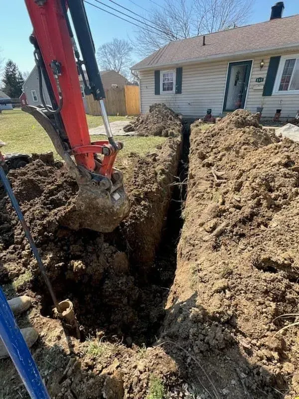 An excavator digging a trench in front of a house. The soil is brown.