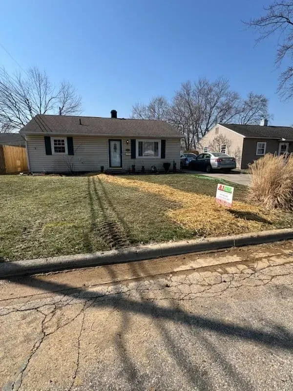Tan brick house with a front yard. Some grass, some mulch. A for sale sign. Sunny day.